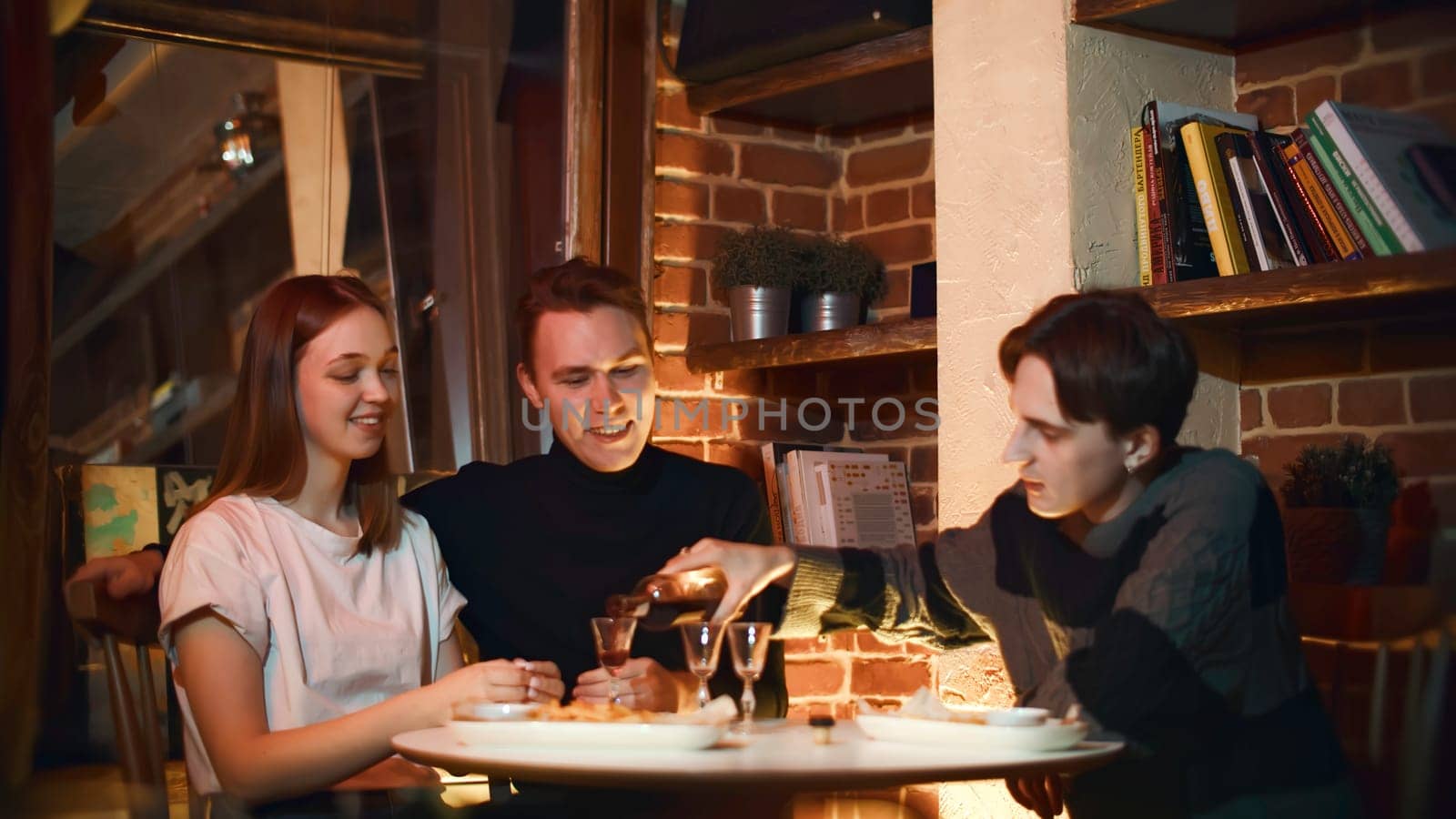 Girl with boyfriend and friend in restaurant. Media. Friends chat in cozy bar with alcoholic drink. Friends have drink in cozy bar on weekend evening.
