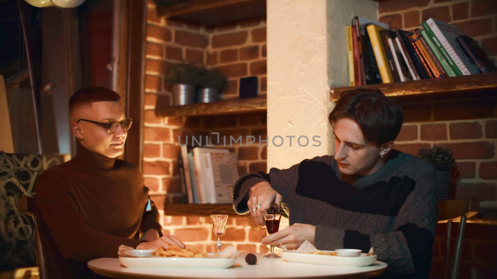 Men drink tincture. Media. Young men are sitting in restaurant, chatting and drinking alcoholic drink. Cozy atmosphere of restaurant with friends and alcoholic drinks.