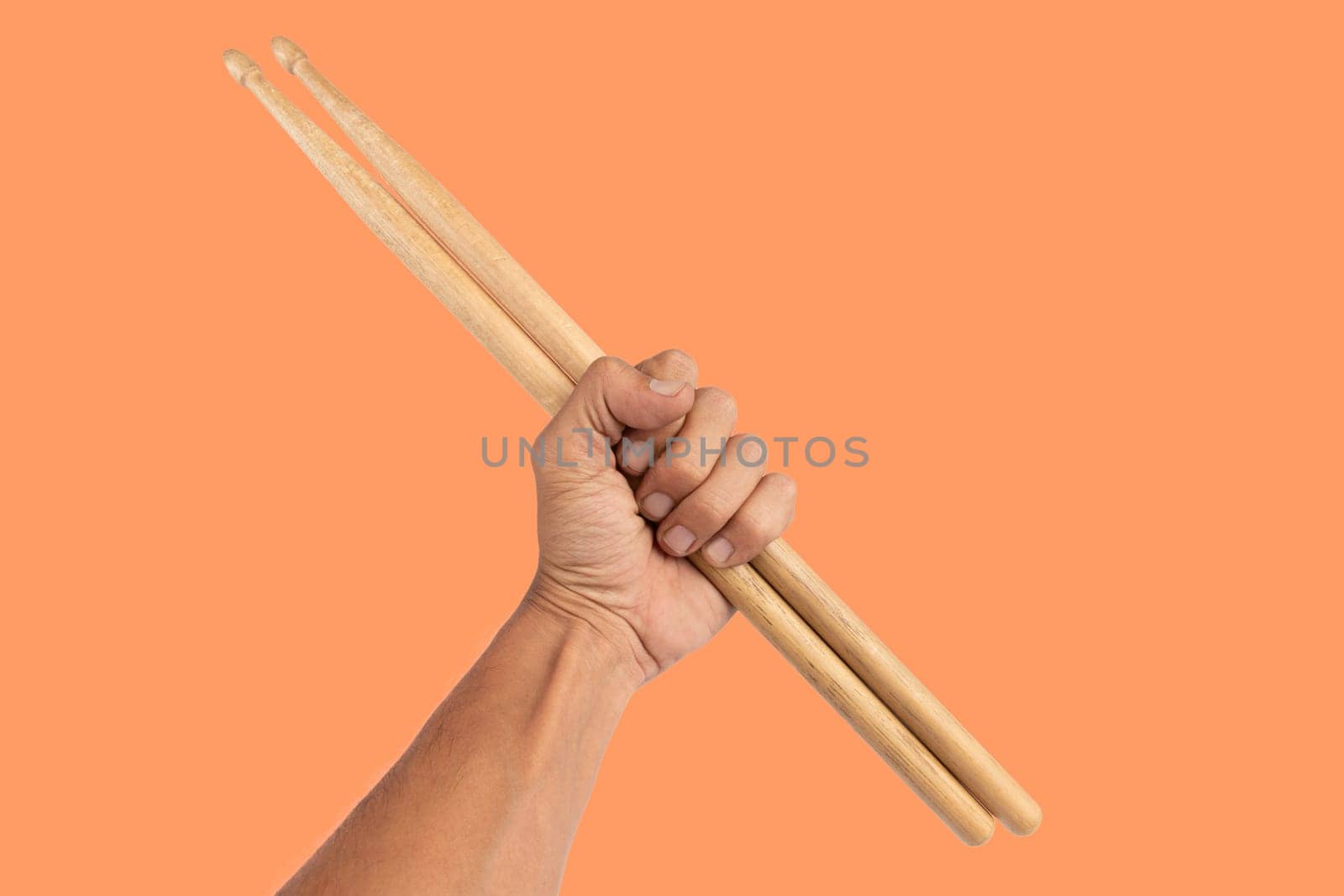 Black male hand holding wooden Drum sticks isolated on orange background by TropicalNinjaStudio