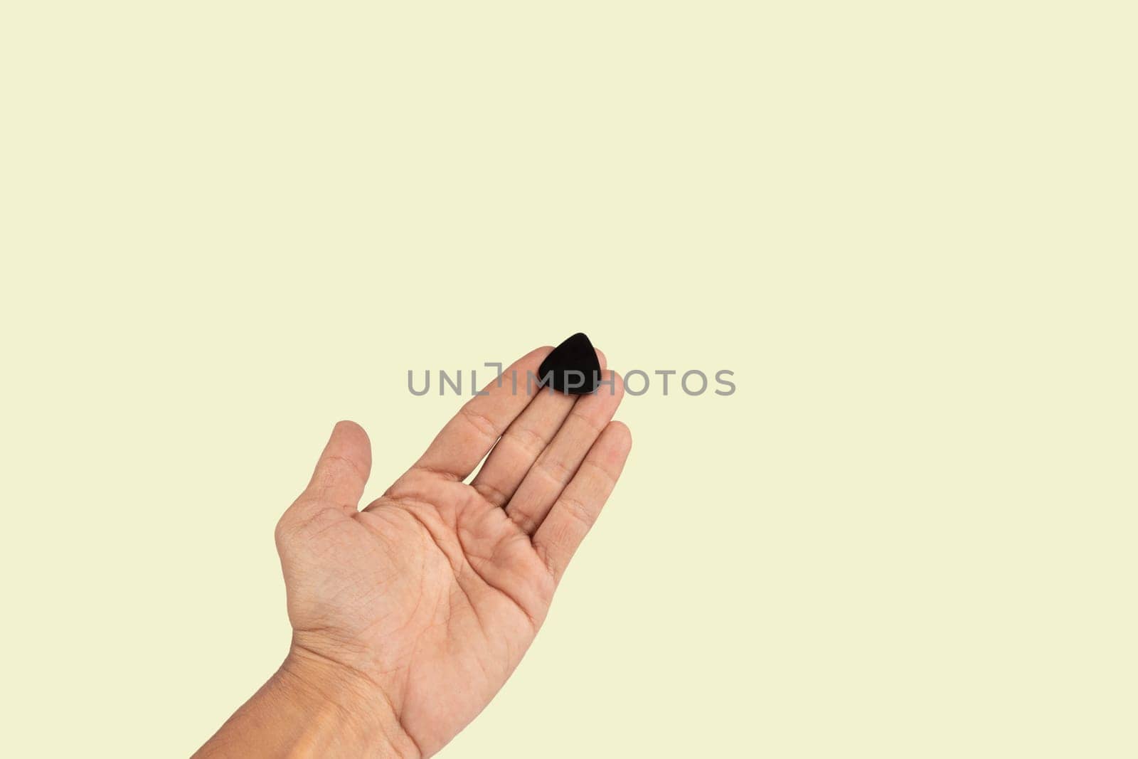 Black male hand holding a guitar pick isolated on light green background. High quality photo