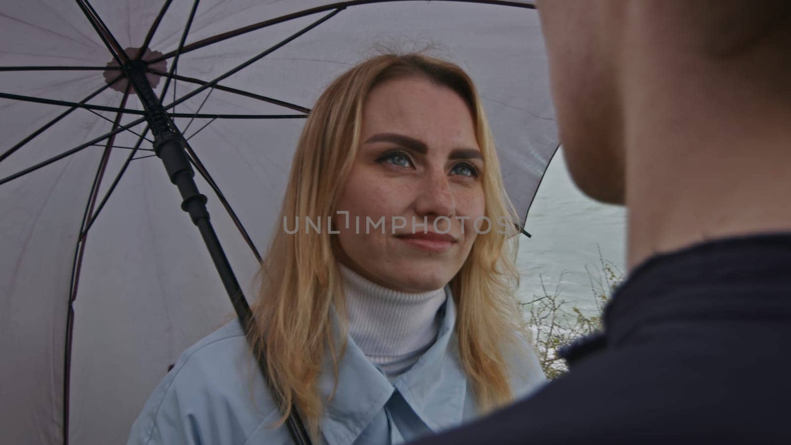 Portrait of a woman with umbrella listening carefully to a man. Stock clip. Romantic couple by the sea on a rainy day