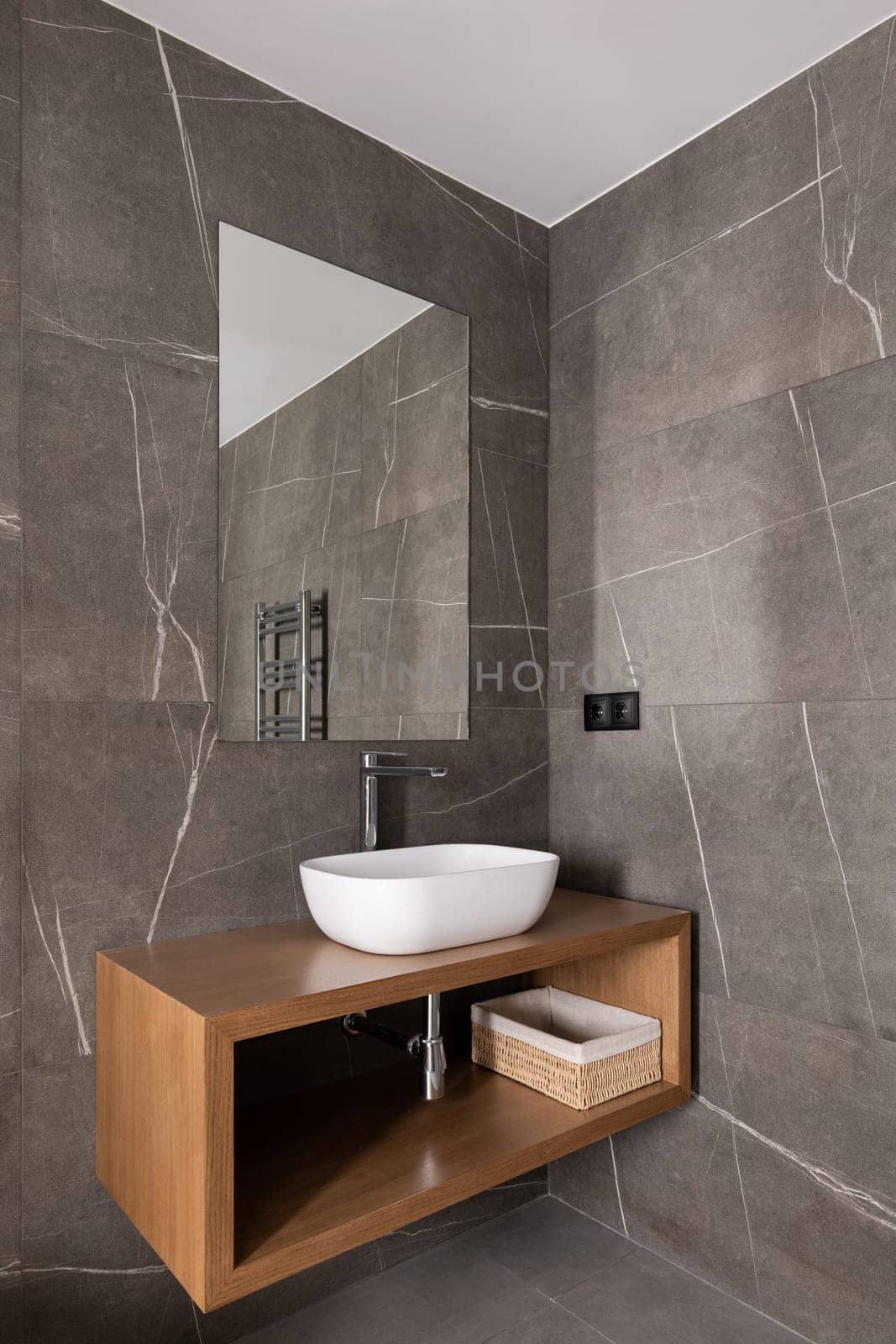 Contemporary bathroom design featuring a wooden vanity with a vessel sink, large mirror, and grey tiled walls.