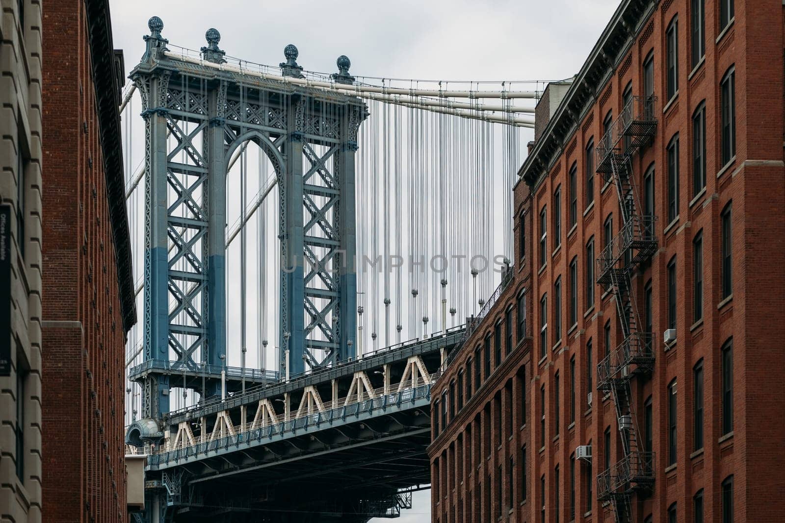 A picturesque view of the iconic Manhattan Bridge framed between two historic red brick buildings in New York City. The scene captures urban architecture and the grandeur of the bridge.