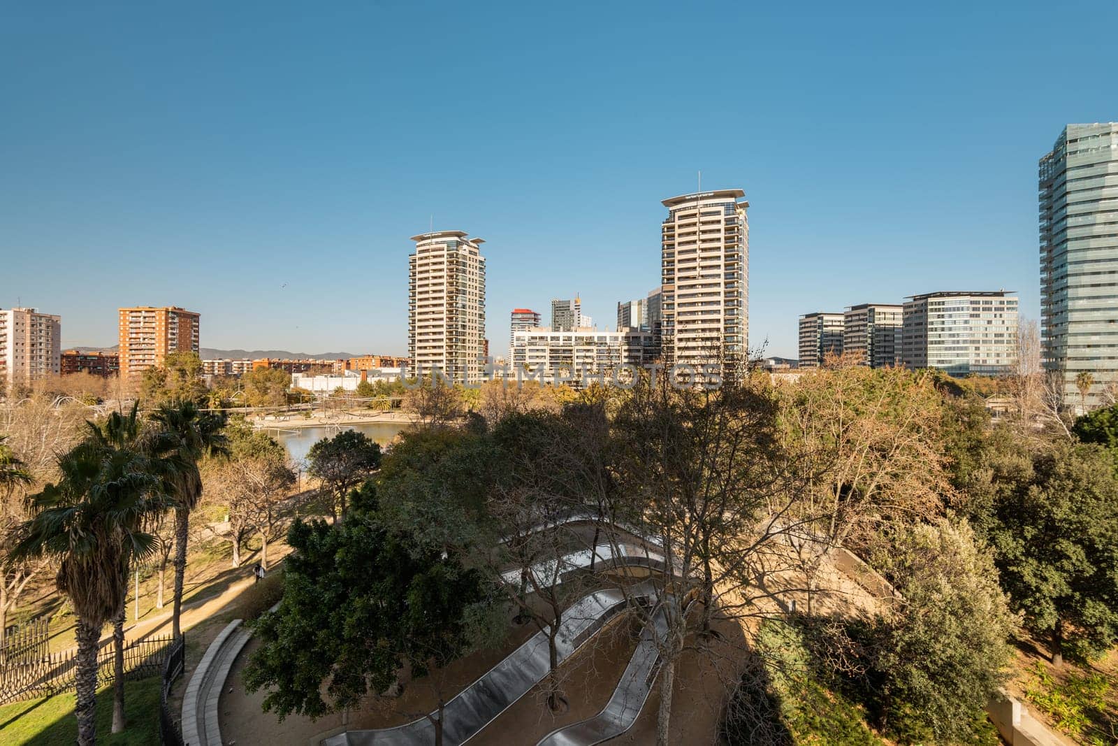 Panoramic view of a city skyline featuring modern high-rise buildings and a green park under a clear blue sky.