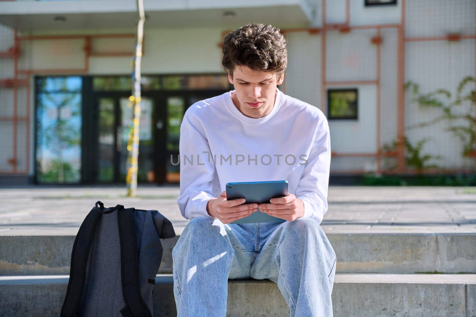 Young handsome guy college student using digital tablet outdoor, educational building background. Education, technology, training, 19,20 years age youth concept