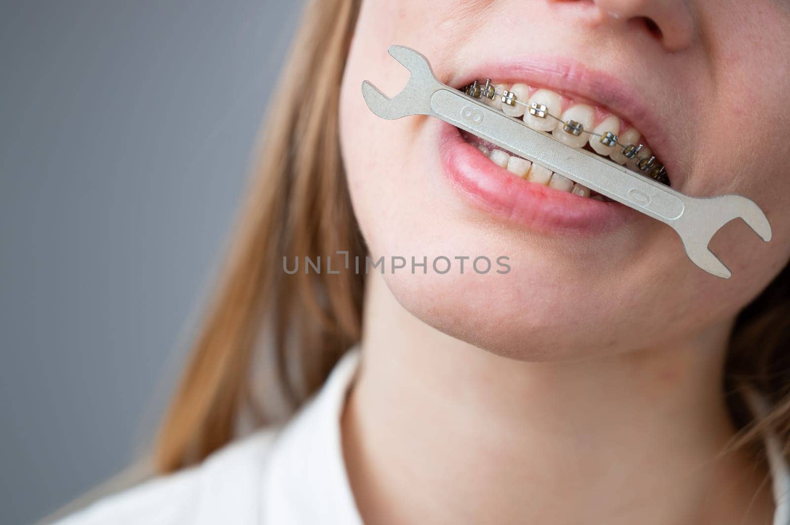 Close-up portrait of a woman with braces holding a wrench in her teeth