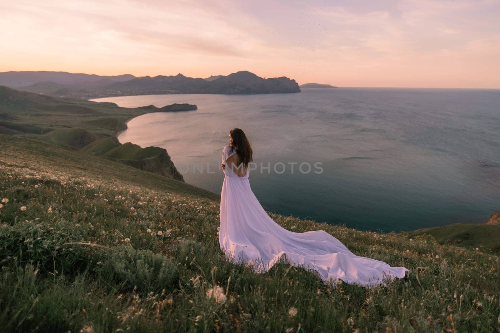 A woman in a white dress stands on a hill overlooking the ocean. The scene is serene and peaceful, with the woman's dress flowing in the wind