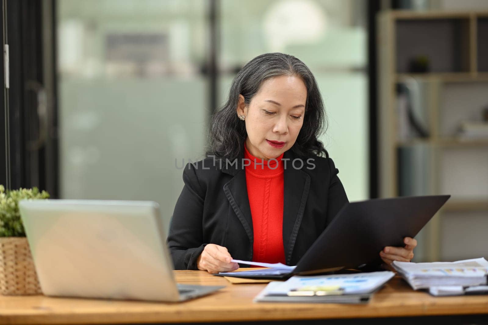 Professional senior woman accounting manager checking financial documents at workplace.