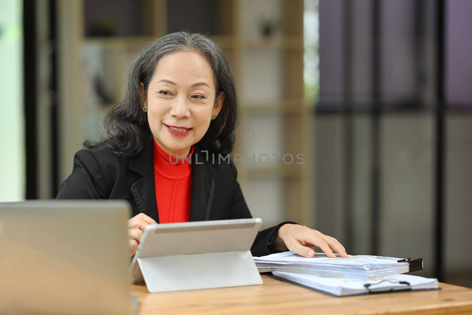 Portrait of smiling mature business woman manager using digital tablet at desk.