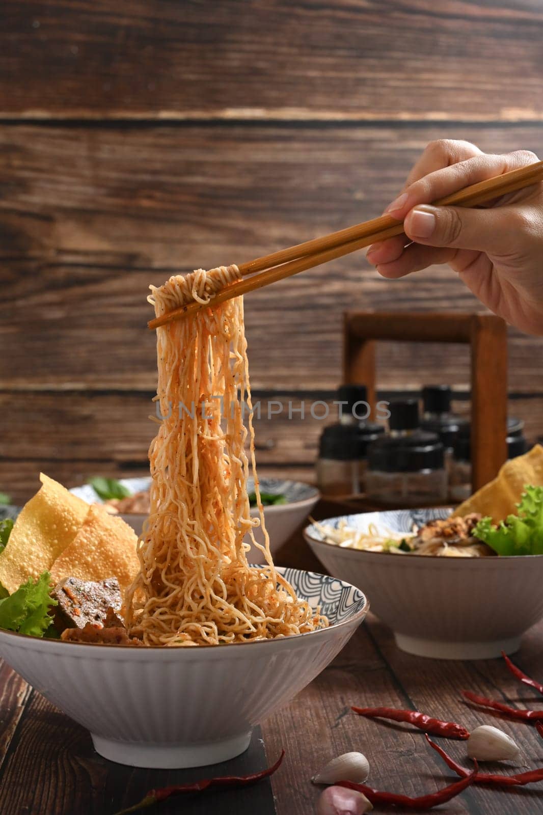 Hand holding spicy egg noodles by chopsticks over wooden rustic background. Asia food and spicy Thai tom yum noodle.