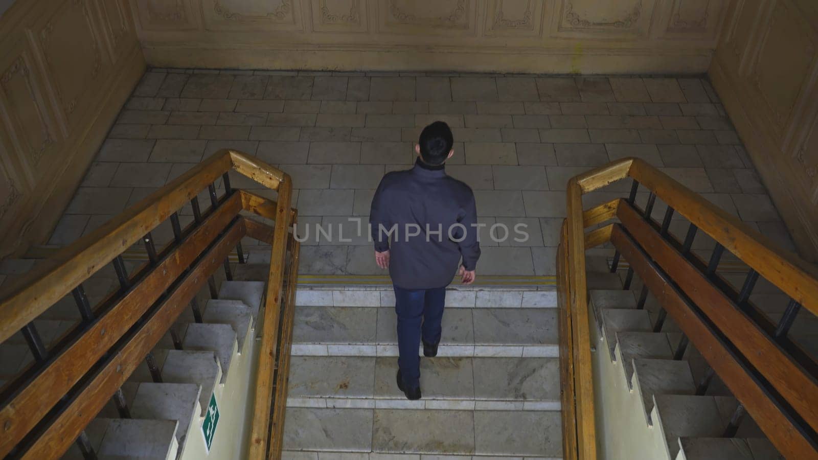 Top view of man walking up stairs of old building. Media. Young man climbs stairs in old university building. Man walks up stairs in theater or university college building.