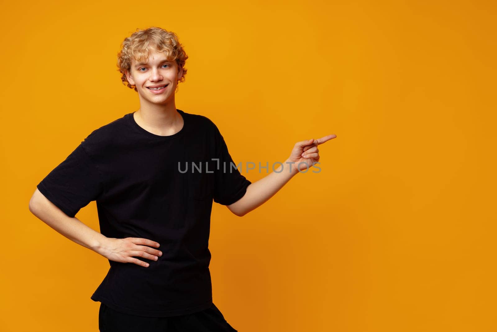 Handsome young man pointing finger to copy space on yellow banner background close up