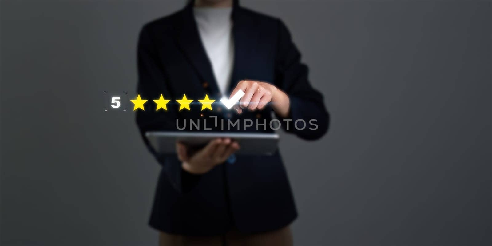 A woman is holding a tablet and pointing to a 5 star rating. Concept of accomplishment and satisfaction, as the woman is giving a thumbs up to the 5 star rating