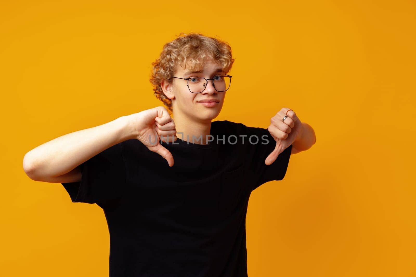 Young man showing thumbs down against yellow background in studio