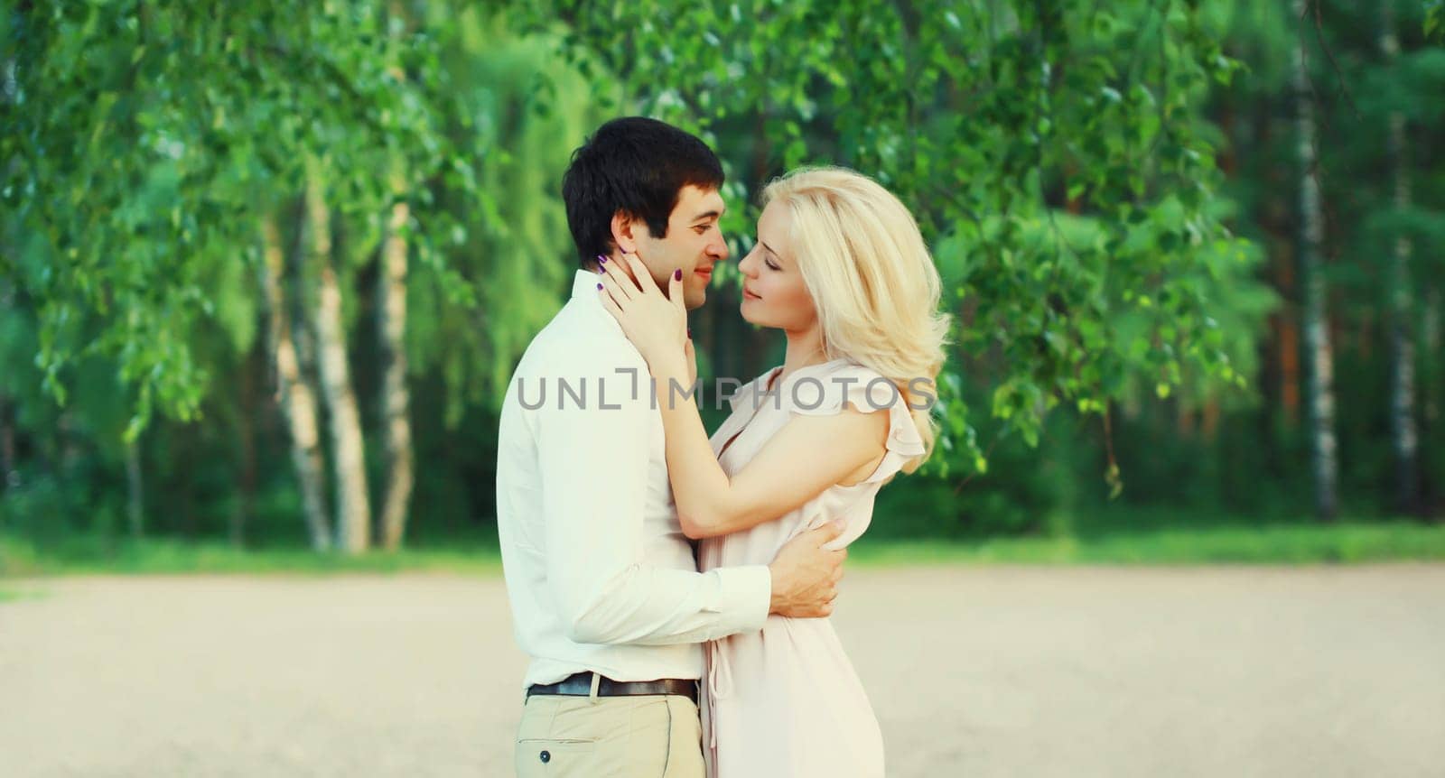Portrait of beautiful happy kissing young couple in love together hugging in green summer park