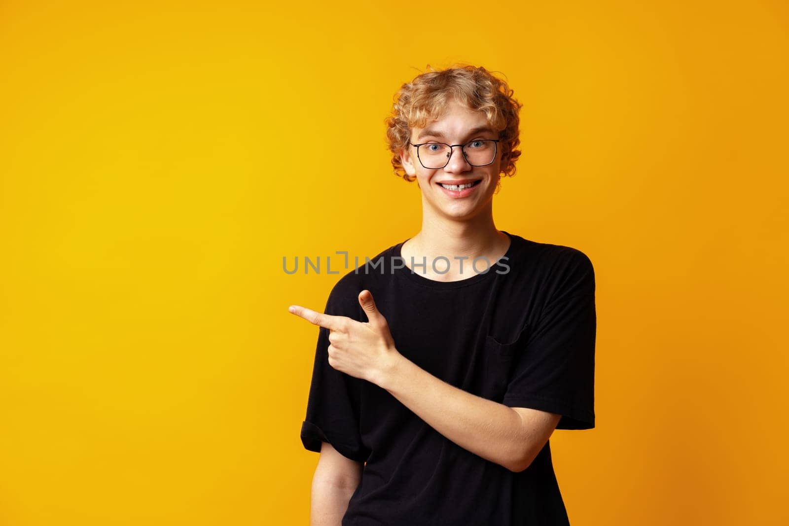 Handsome young man pointing finger to copy space on yellow banner background close up