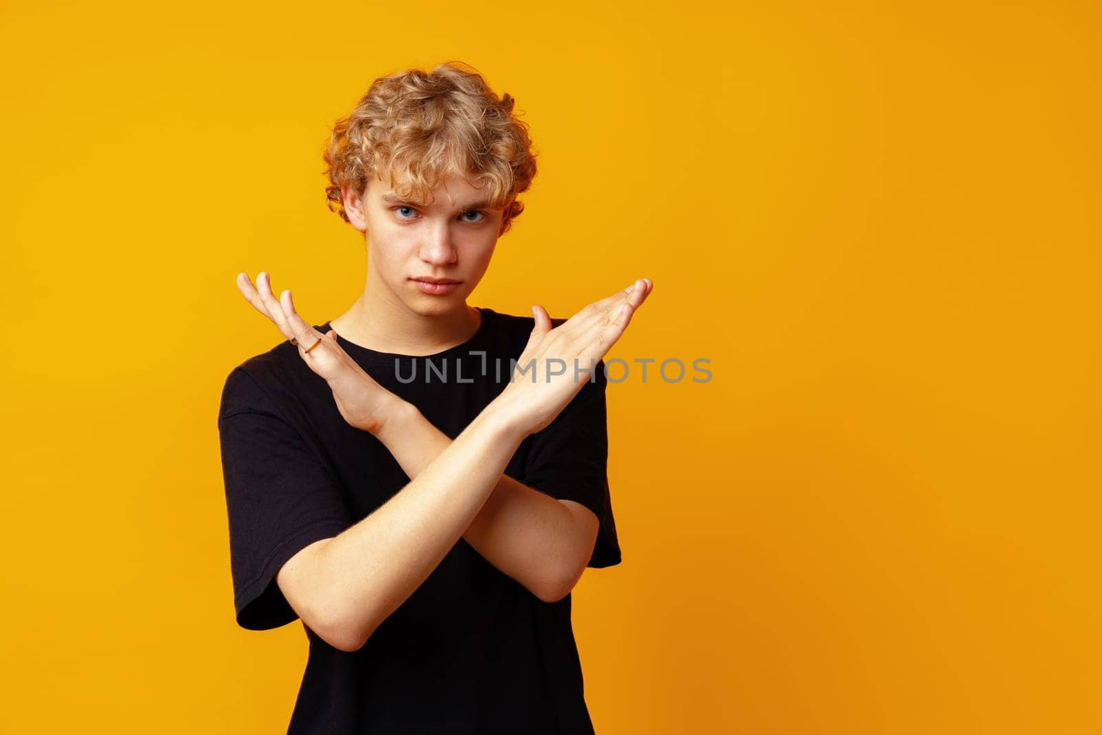 Photo of young strict man showing arms denial symbol against yellow background close up