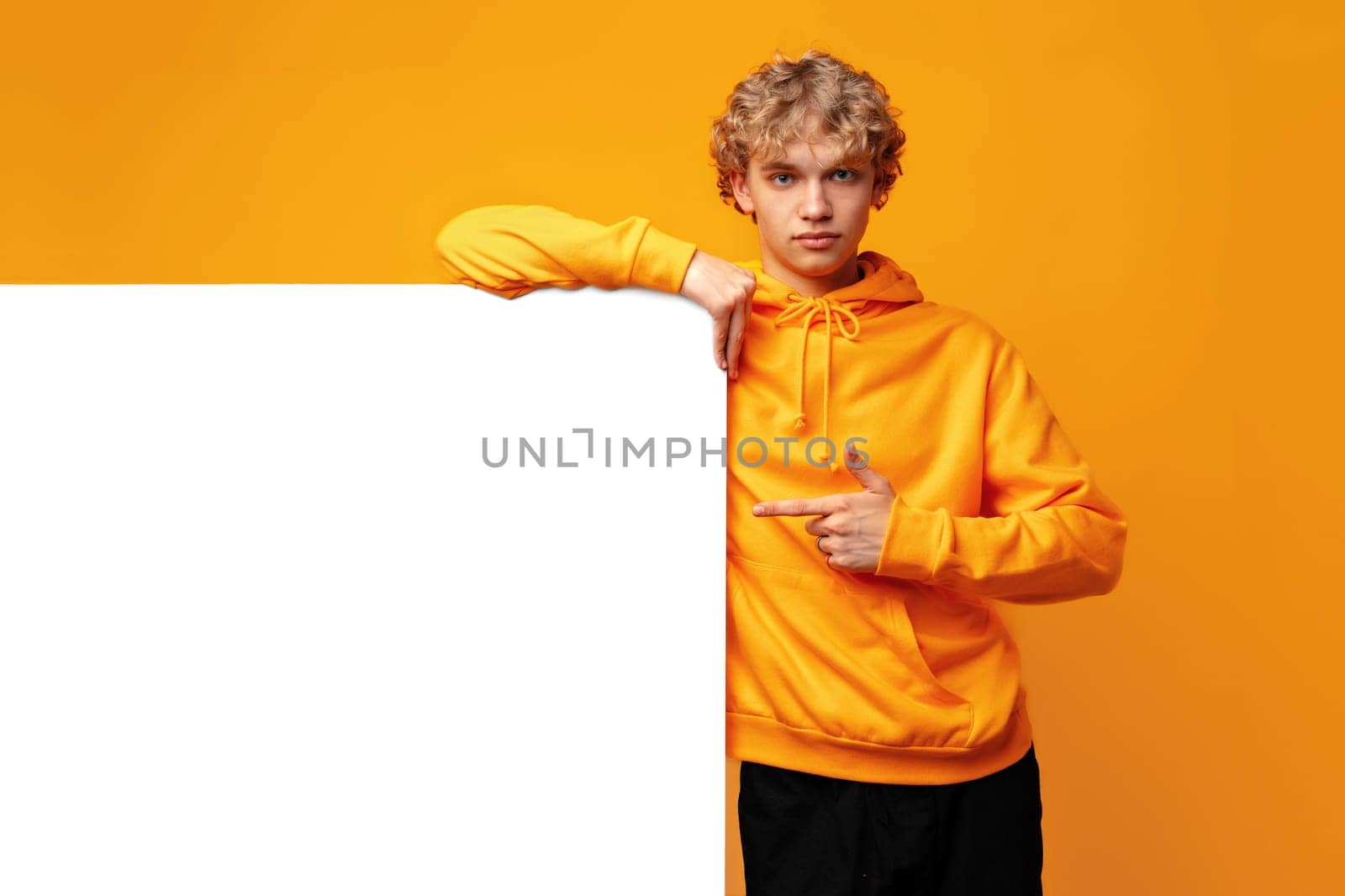 Young man holding a blank panel for advertising against yellow background, copy space