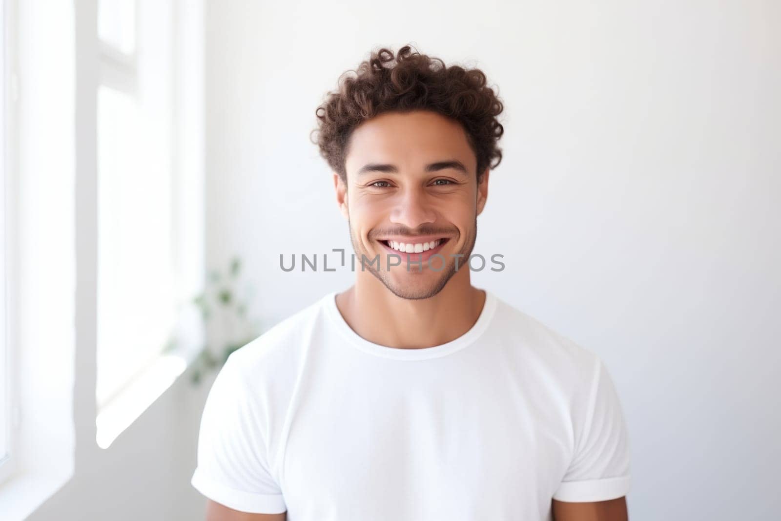 Portrait of handsome happy smiling young man in t-shirt with toothy smile looking at camera in white room at home