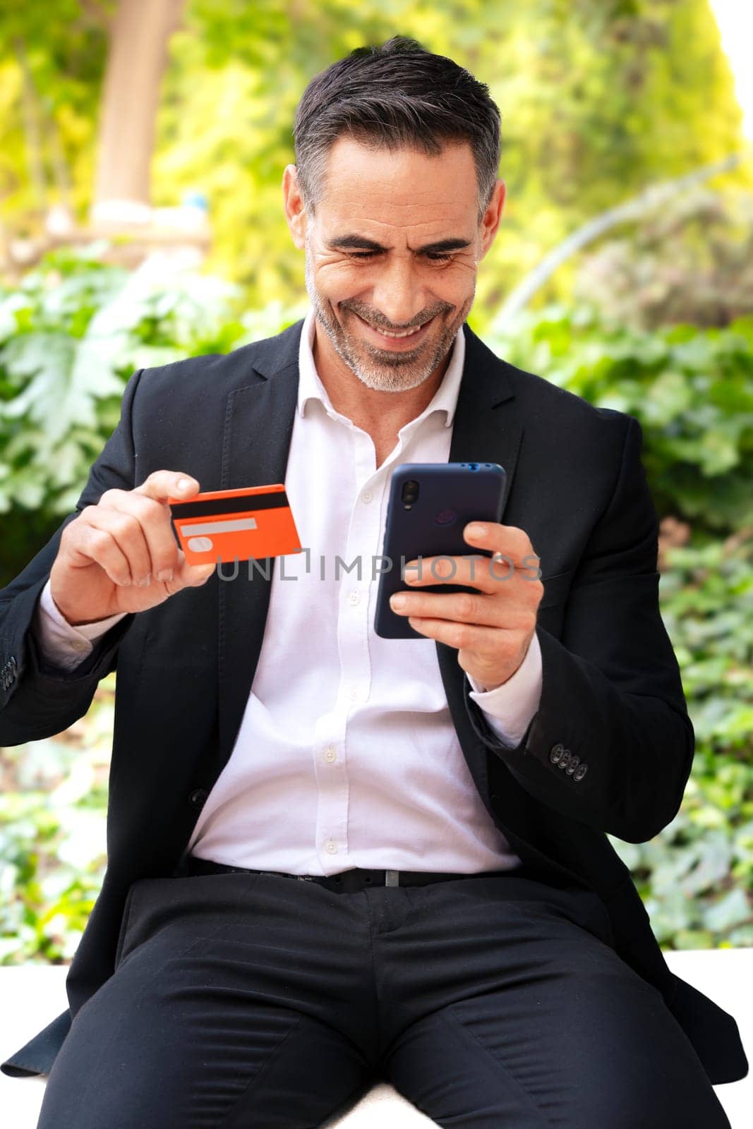 Vertical portrait man with credit card and cell phone in his hands outdoors. Concept: Online Shopping.