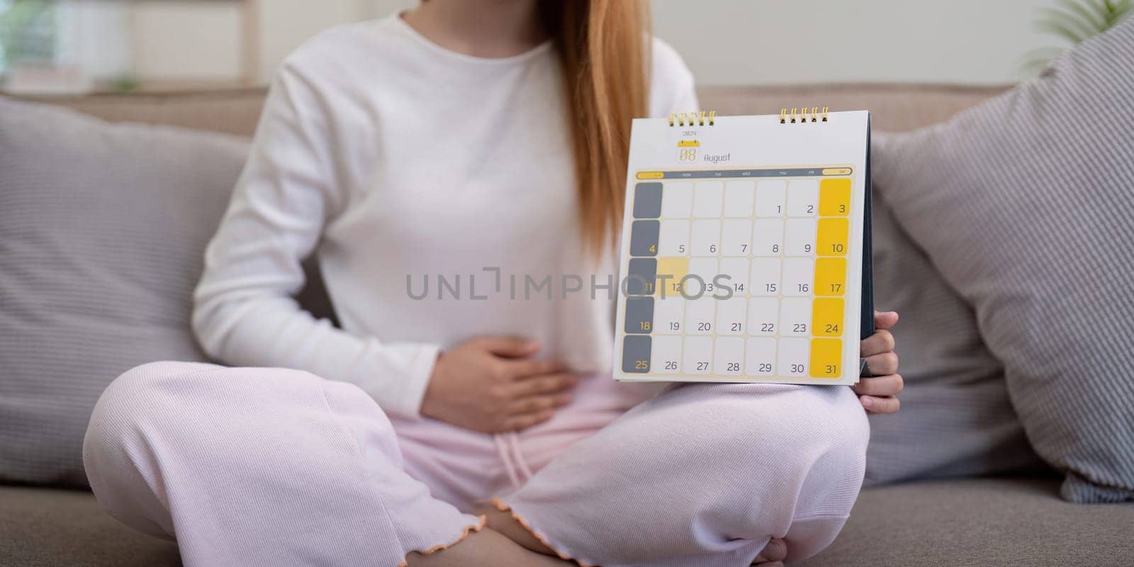 Woman sitting with a calendar and holding her stomach. Concept of menstrual cycle tracking and health.