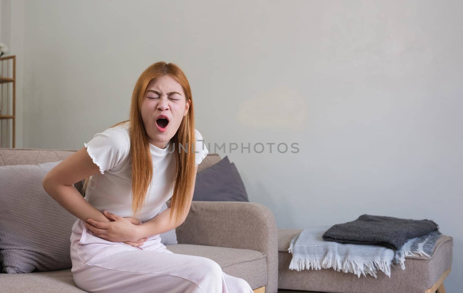 A young woman with stomach pain from diarrhea or menstrual cramps felt sick and touched her stomach with an unhappy expression..