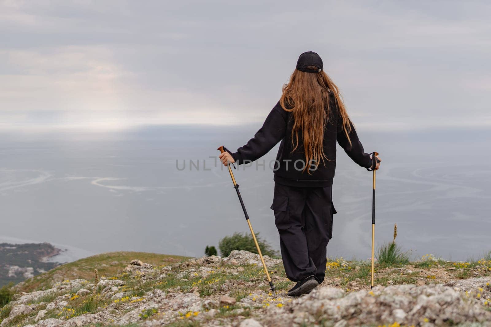 A woman with long hair is standing on a hill overlooking the ocean by Matiunina