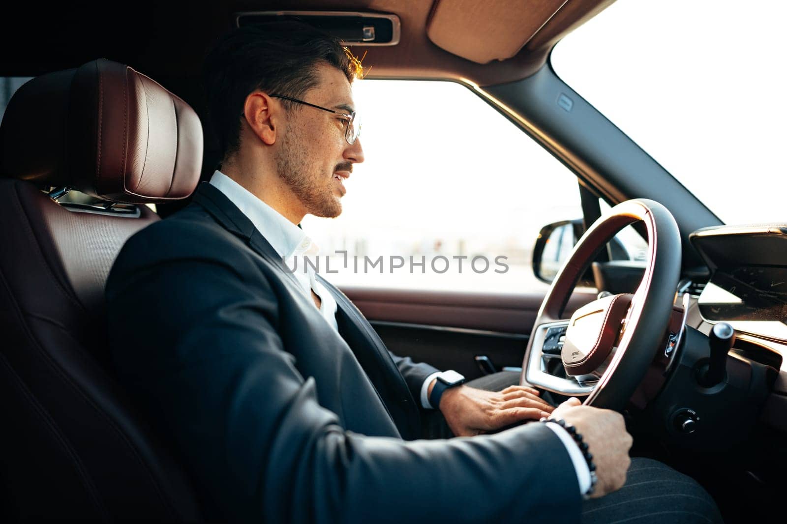 Young businessman in elegant suit driving luxury car close up