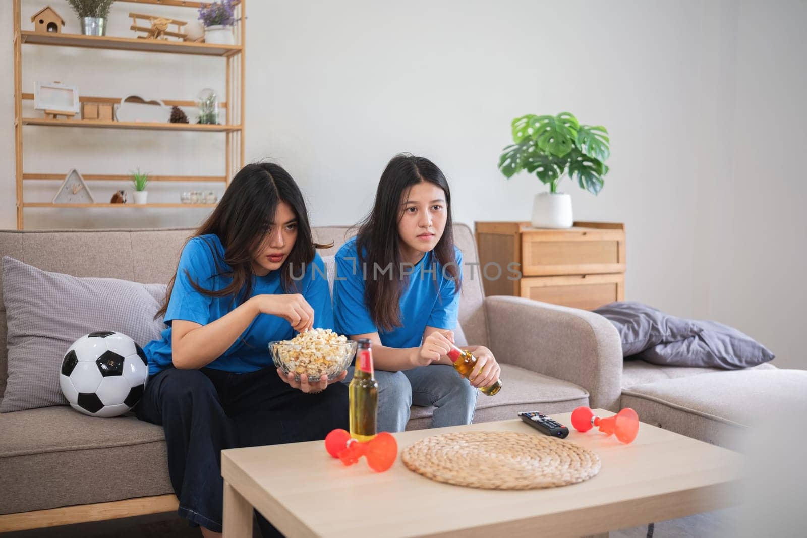 Asian women intently watching soccer game at home. Concept of sports, focus, and friendship by wichayada