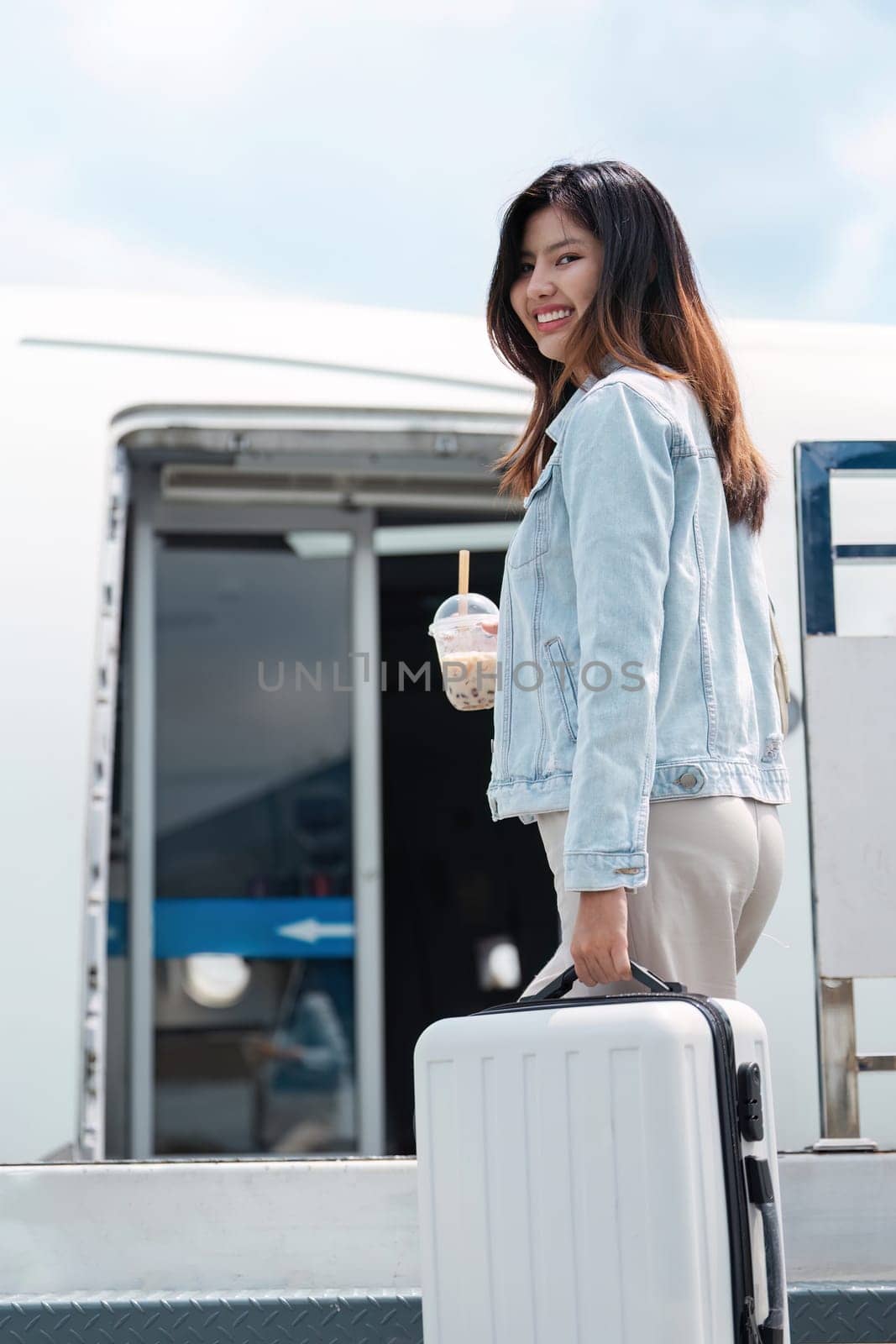 A woman is smiling and holding a cup of coffee while standing next to a suitcase. Concept of travel and adventure, as the woman is preparing to embark on a journey