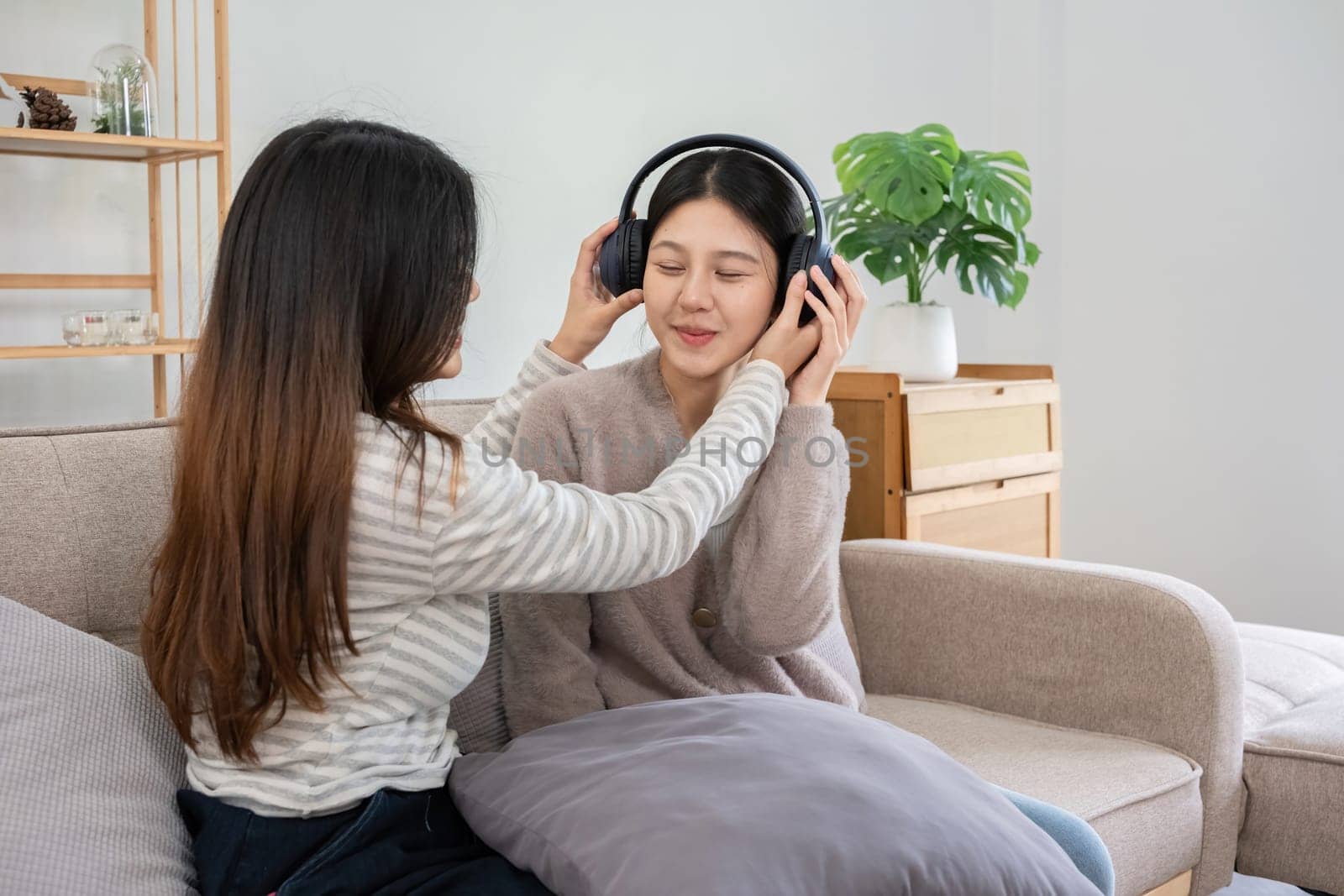 Asian lesbian couple enjoying music together at home. Concept of love, bonding, and leisure in a cozy indoor setting.