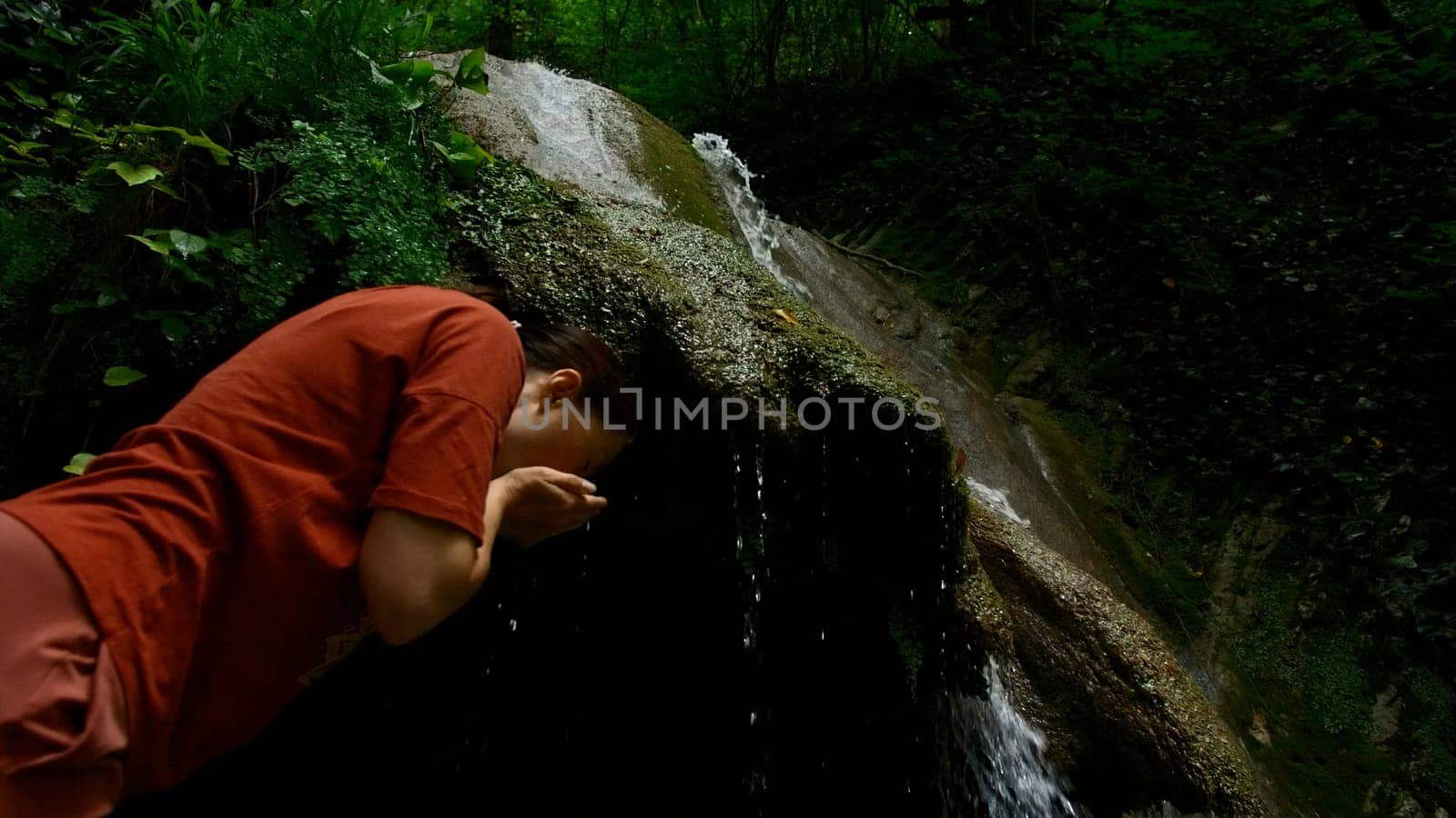 Young woman drinking water from cascade waterfall at deep tropical rain forest. Creative. Female hiker drinking water from mountainous spring