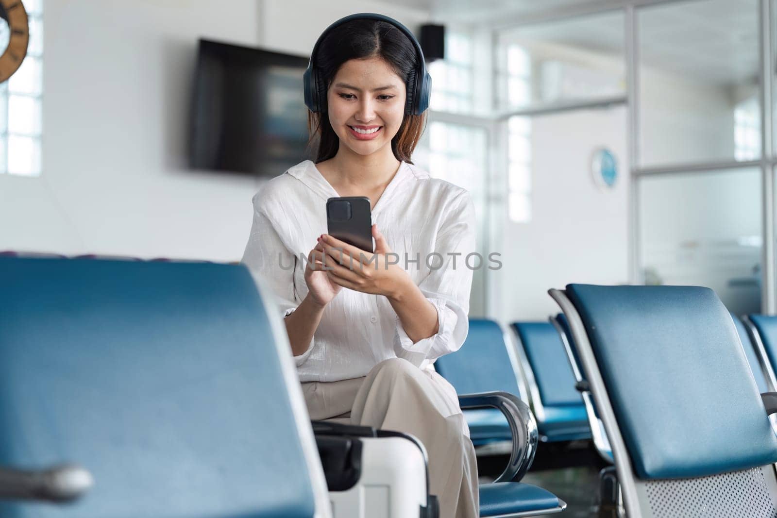 Woman listening to music on headphones in airport lounge, use smartphone and earphones while waiting for her flight.