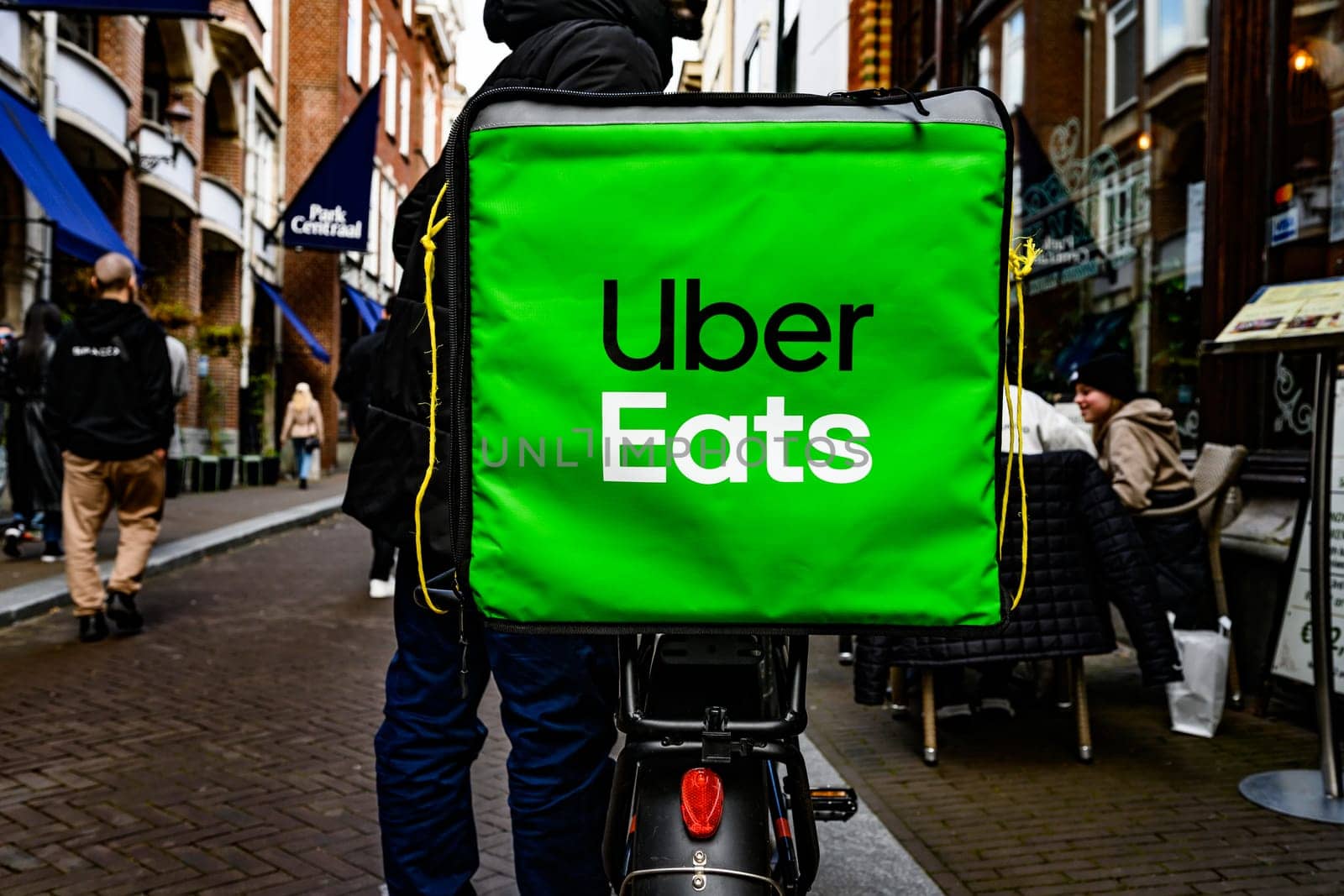 Hague, Netherland - 09 April 2023: Big green Uber Eats Food Bag. Food delivery man by bicycle