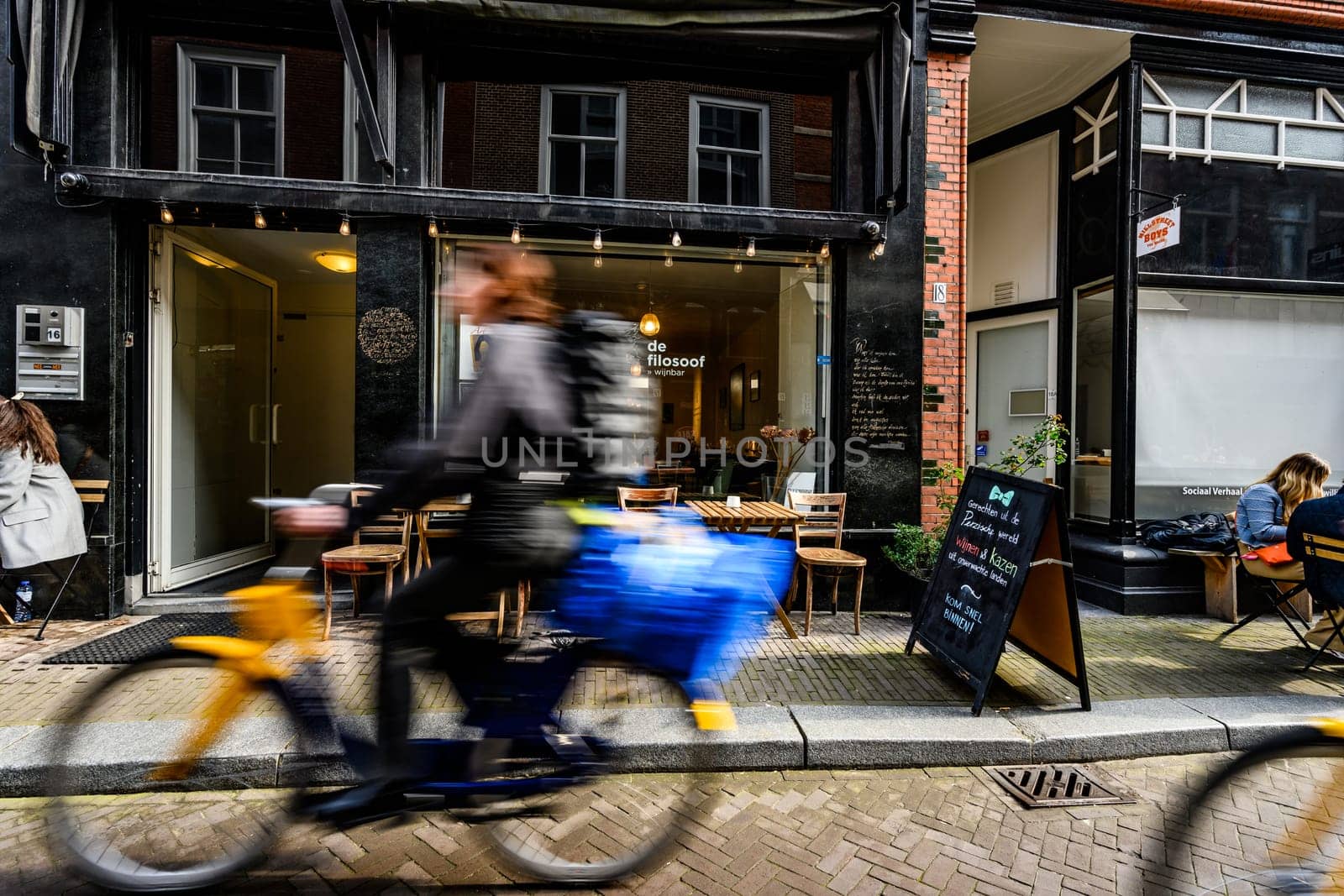 Hague, Netherland - 09 April 2023: Blurry bikers on a street of Hague. Cozy Cafe in the center of a touristic place in Holland.