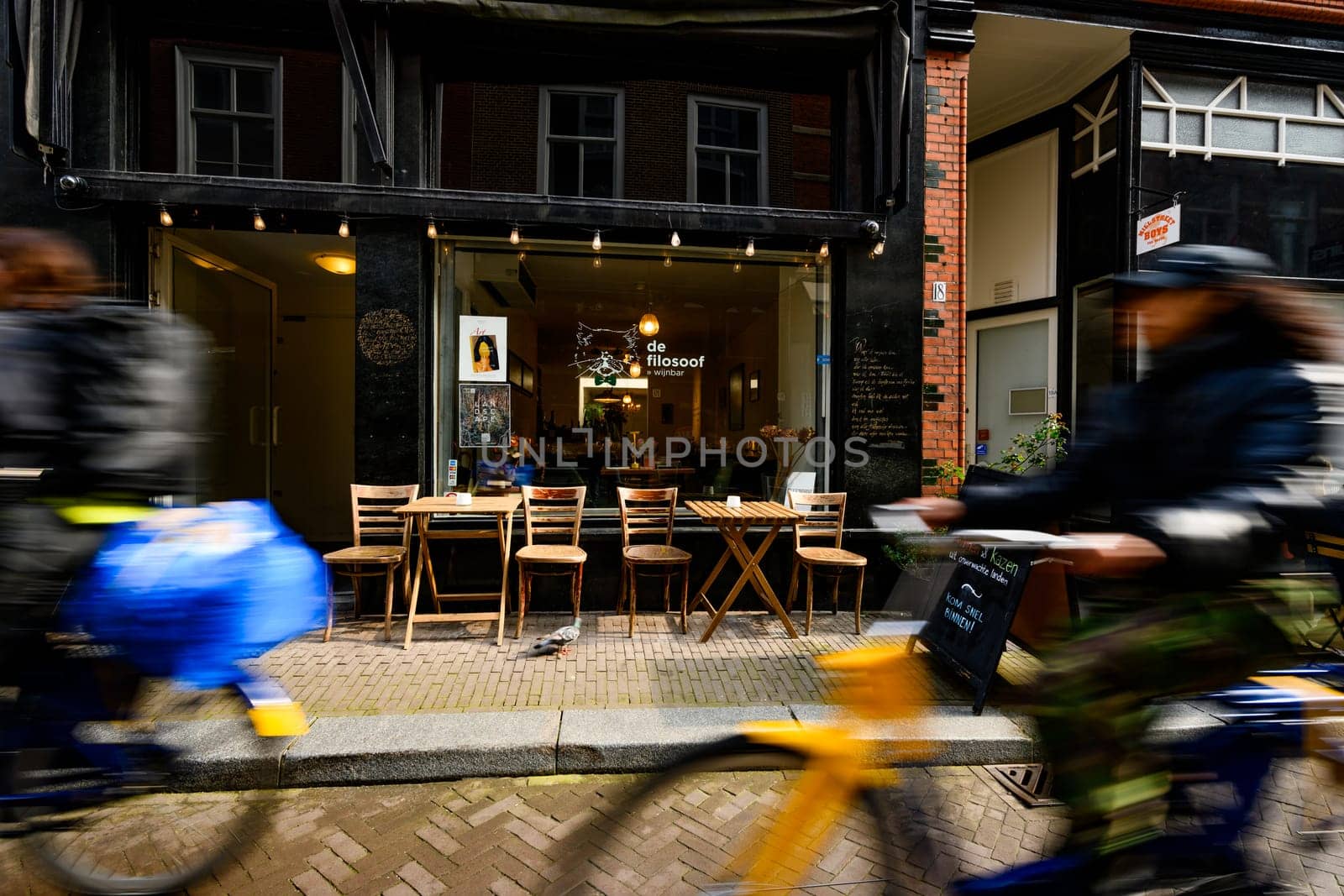 Hague, Netherland - 09 April 2023: Blurry bikers on a street of Hague. Cozy Cafe in the center of a touristic place in Holland.