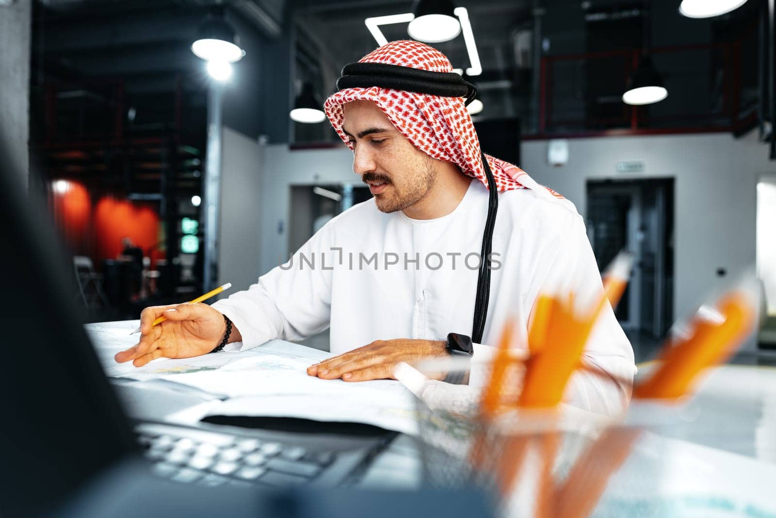 Young muslim businessman in traditional outfit working at the table in office clsoe up