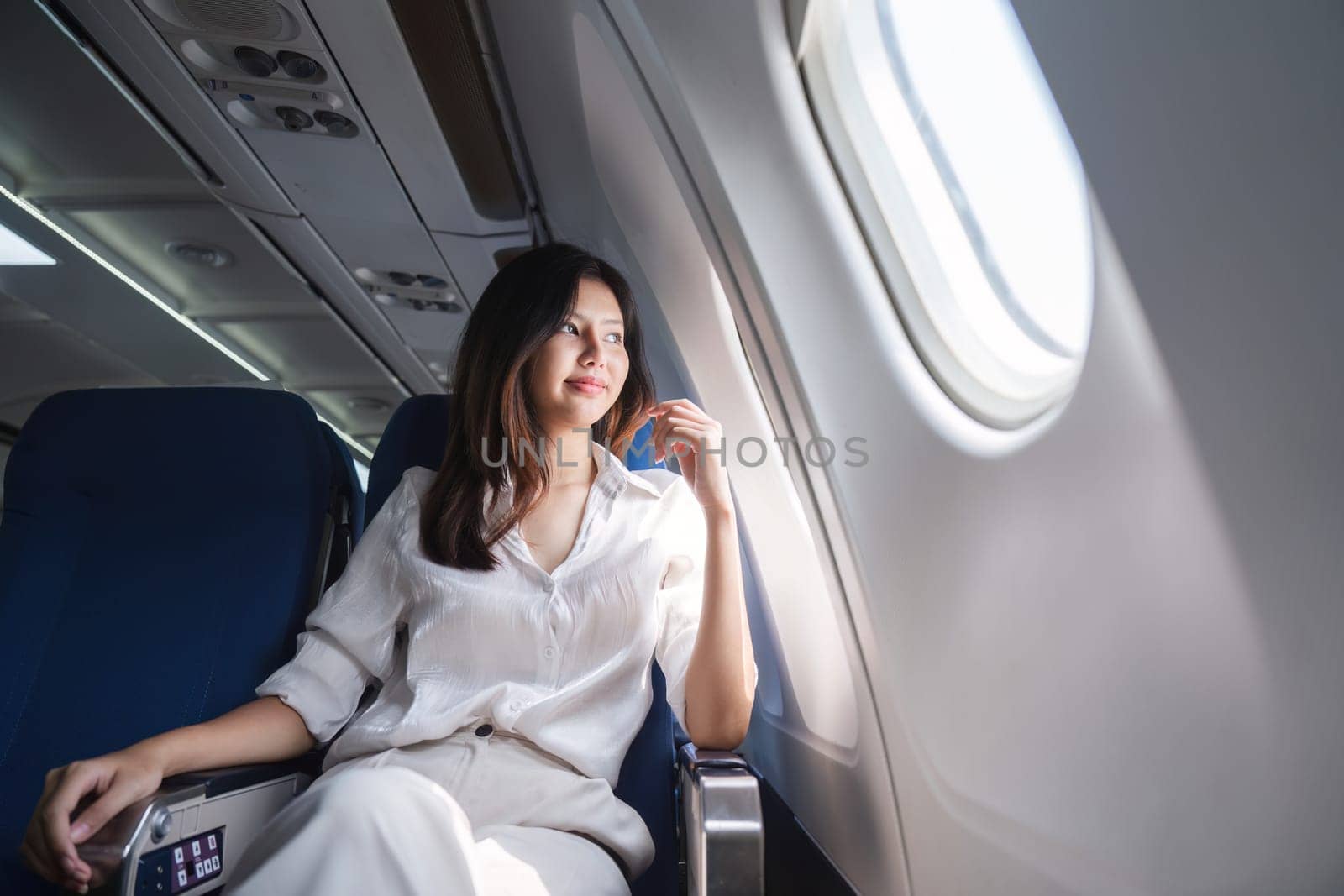 Asian woman looking out airplane window during flight.