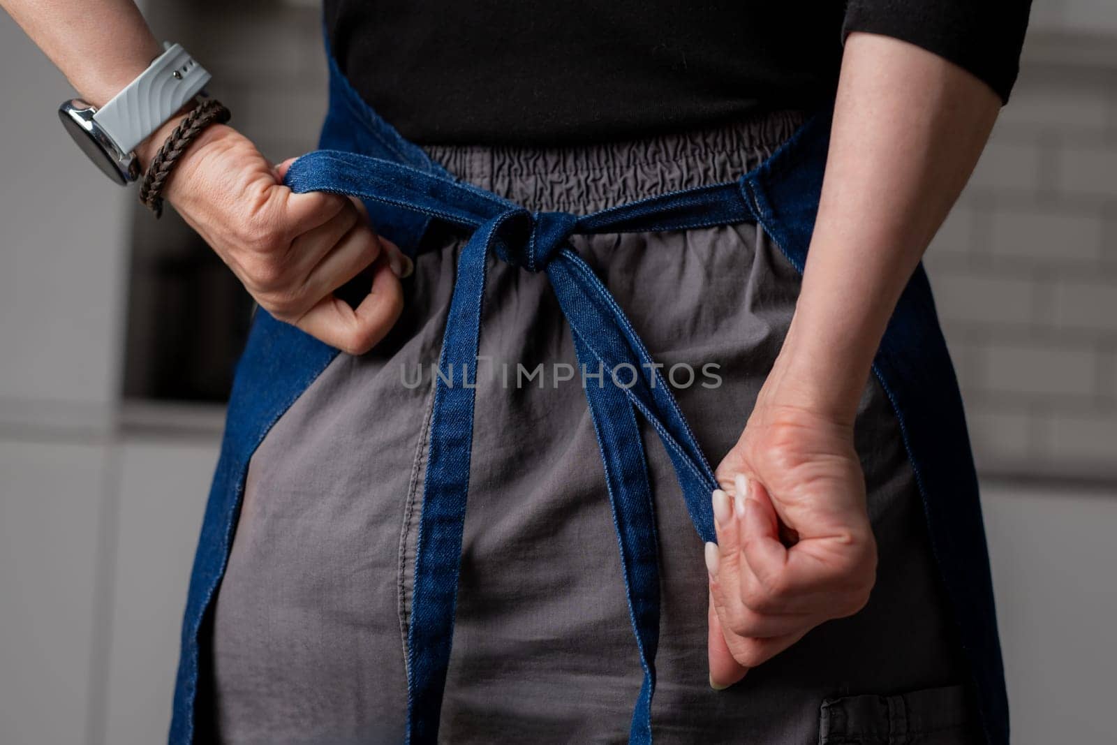 Female Hands Are Tying A Kitchen Apron Behind In Close-Up View