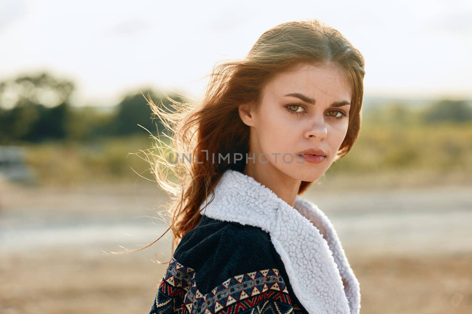 Serene young woman with flowing brown hair gazes at the camera in a picturesque field setting