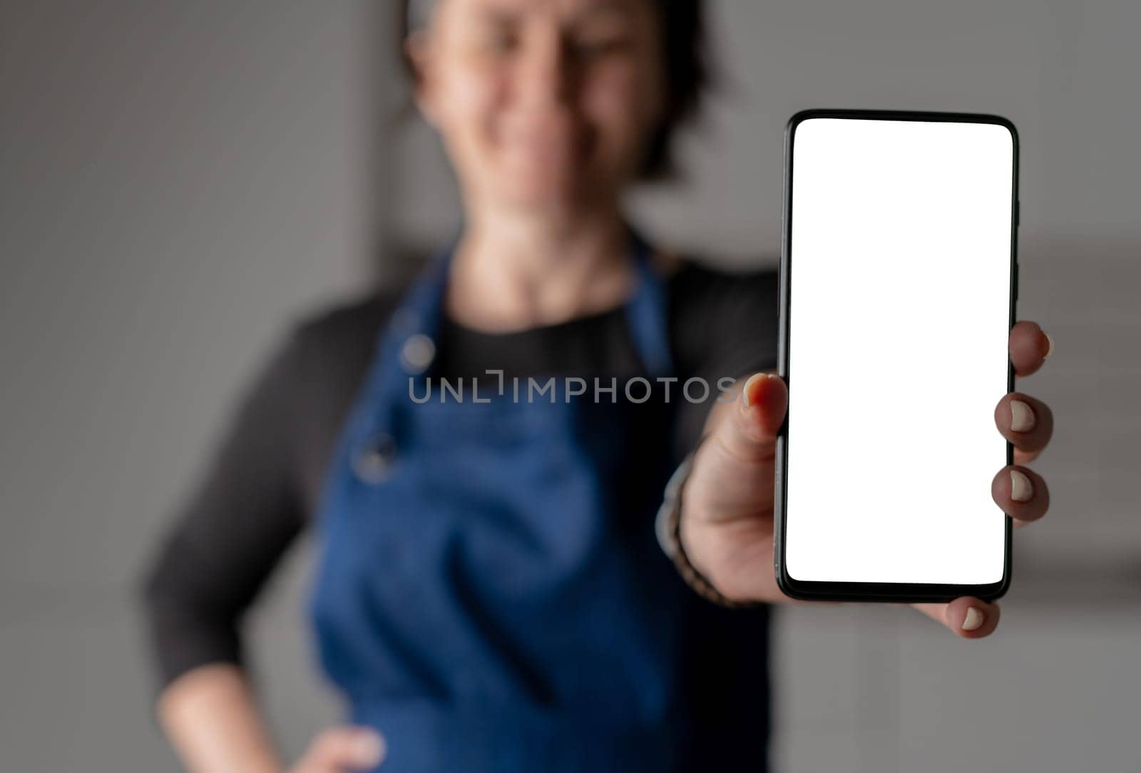 Woman In Apron Showing Smartphone With White Screen by tan4ikk1