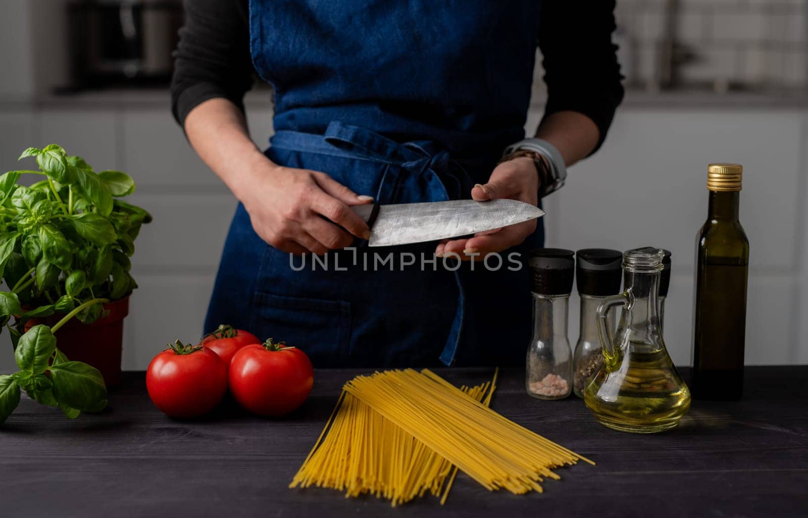Housewife Checks Knife Sharpness Close Up Near Table With Tomatoes, Pasta, Greens