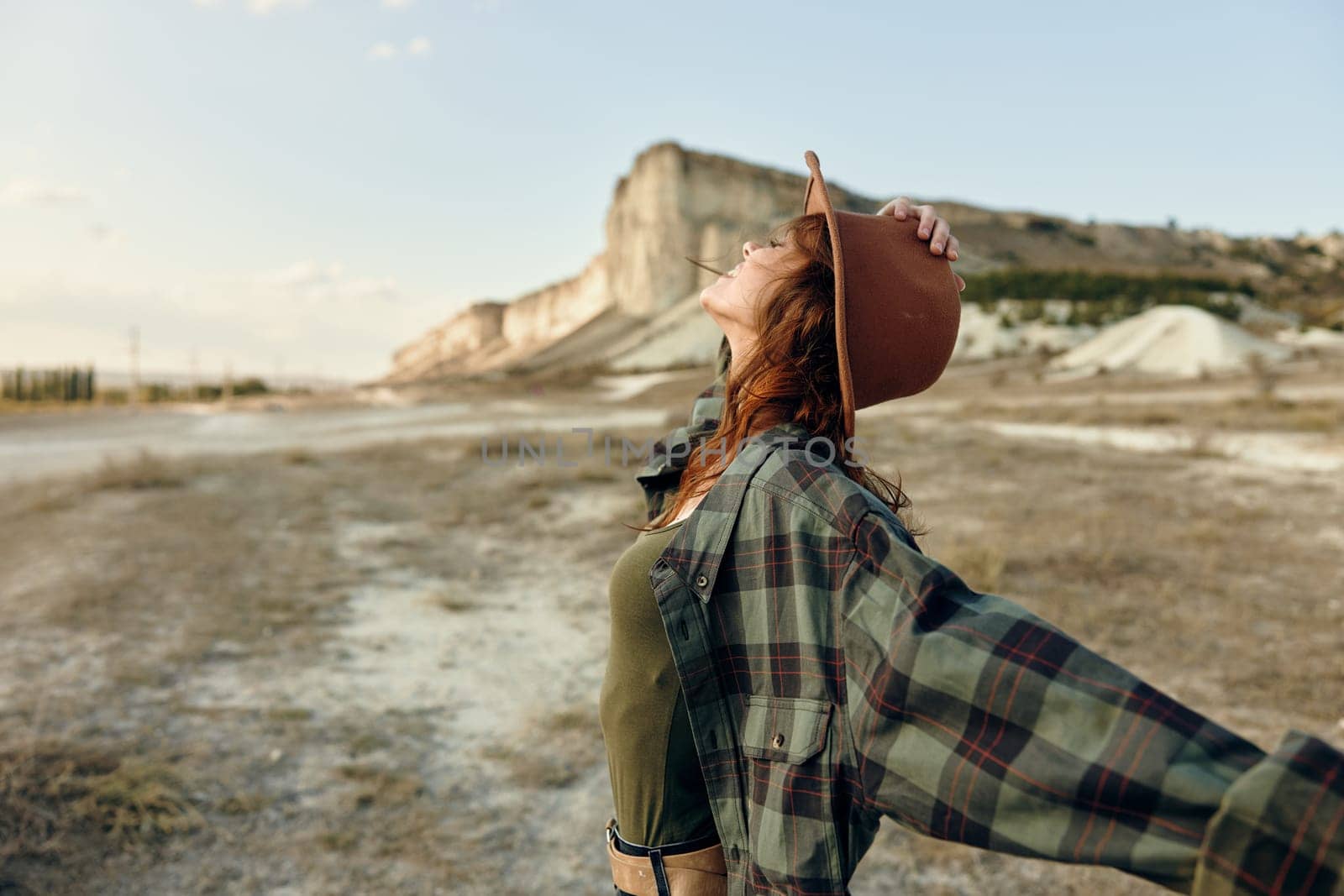 Woman in plaid shirt and hat embracing the mountain majesty with arms outstretched
