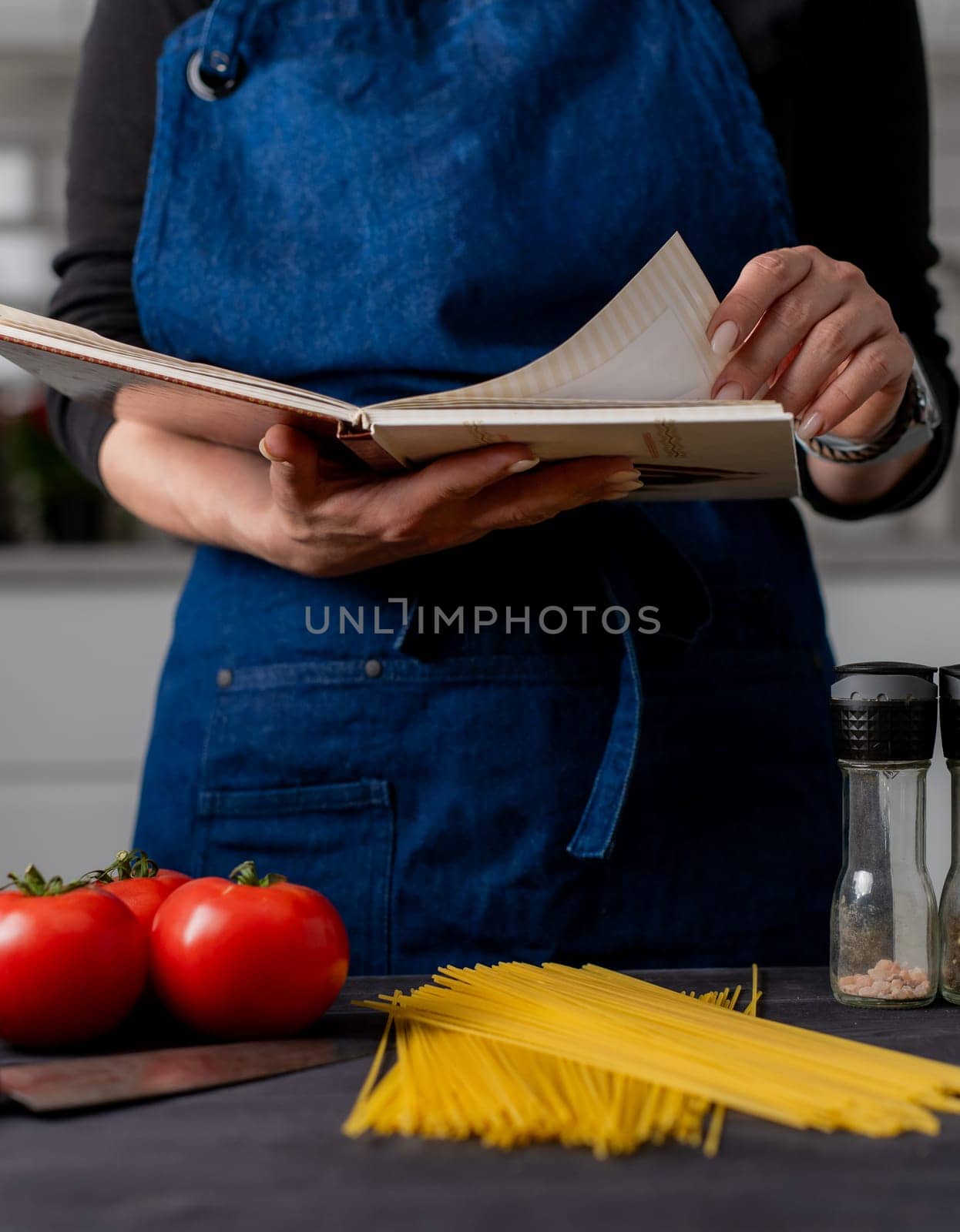 Woman'S Hands With A Recipe Book Hover Over A Table With Spaghetti, Tomatoes, Spices, And Basil