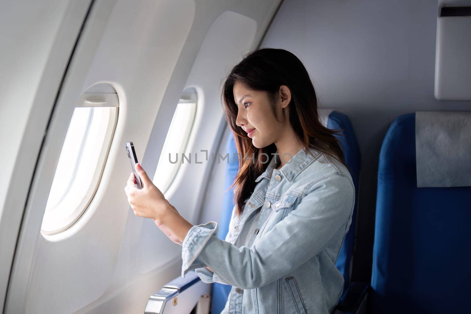 Asian woman taking photo out airplane window during flight.