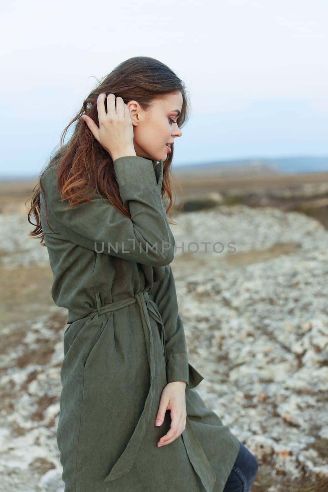 Mystery woman in olive green trench coat gazing at rocky horizon from hilltop by Vichizh