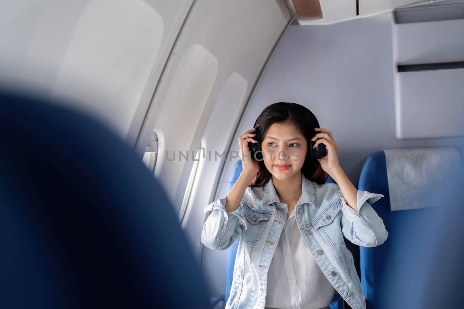 Asian woman listening to music with headphones on airplane during flight.