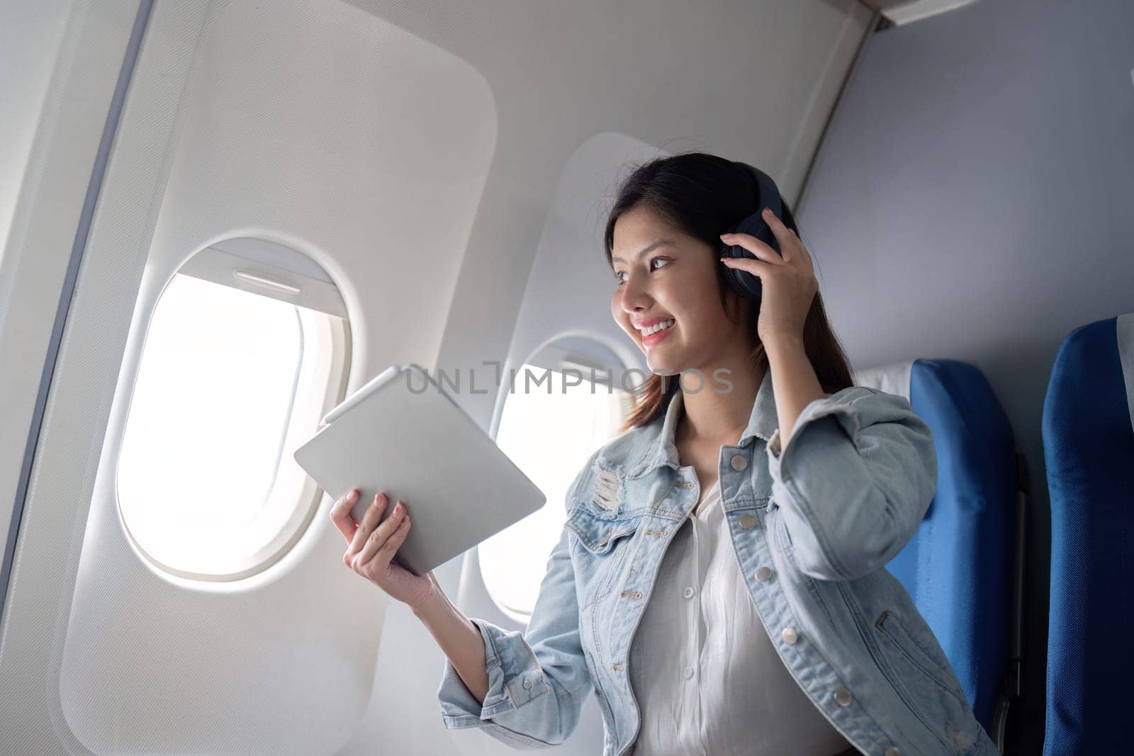 Asian woman using tablet and headphones on airplane during flight.