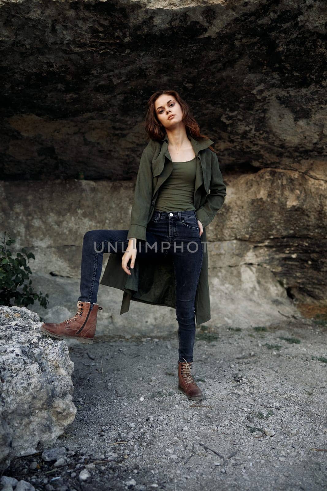 Woman in green coat standing in front of majestic rock formation on a clear day