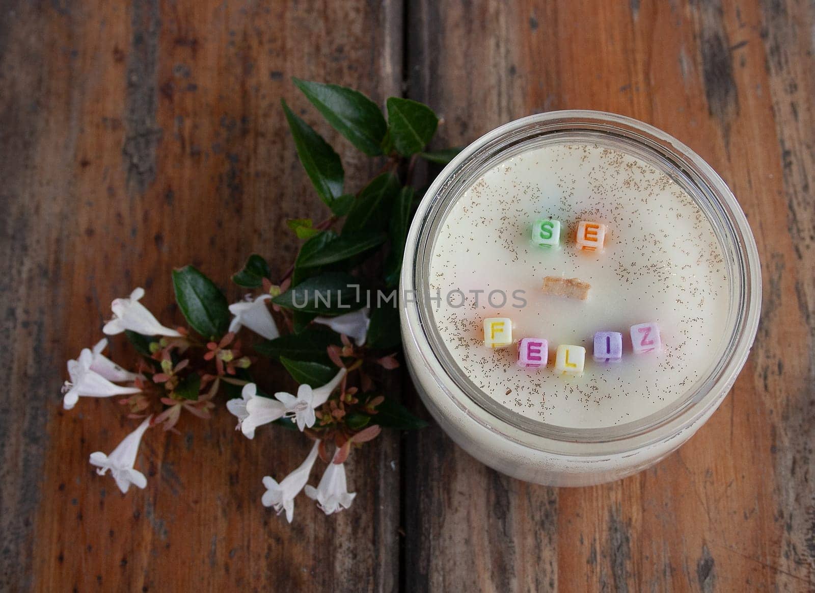 Vanilla scented candle and white flowers on a wooden table.Be happy message by VeroDibe